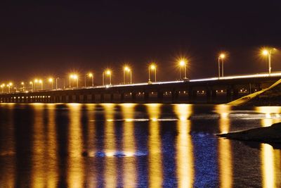 Illuminated bridge over river against sky at night