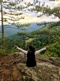 Woman with arms raised in forest against sky