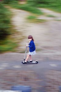 High angle view of cute girl riding push scooter on footpath