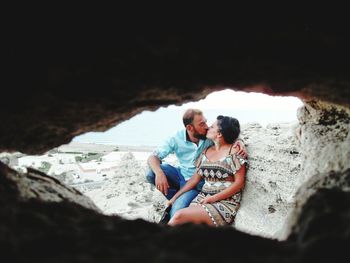 Couple kissing by rock formation at beach seen through cave