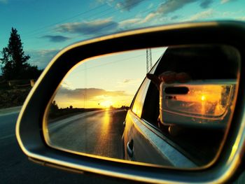 Reflection of car on side-view mirror against sunset sky