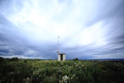 Lighthouse on field against cloudy sky