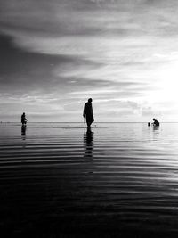 Silhouette people standing at beach against sky during sunset