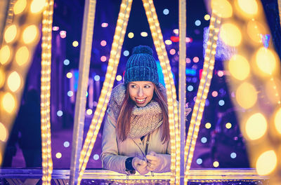 Beautiful woman wearing knit hat smiling by illuminated lights at night