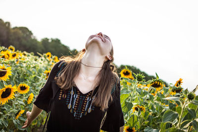 Woman standing by sunflower plants against sky