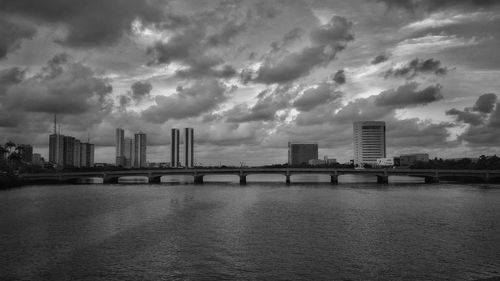 Bridge over river by buildings against sky