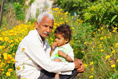 A senior farmer and a young little child eating fruits in the marigold garden, india