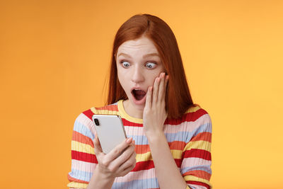 Portrait of beautiful young woman using smart phone against orange background