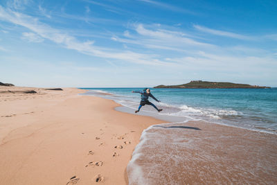 Rear view of woman walking at beach against sky