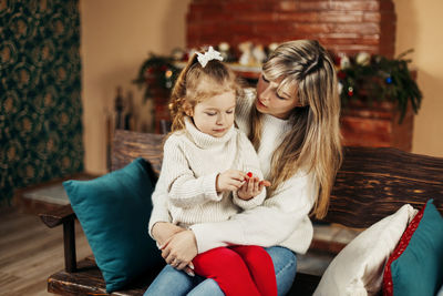 Smiling mother and daughter sitting on sofa at home