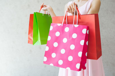 Midsection of woman holding umbrella against pink wall