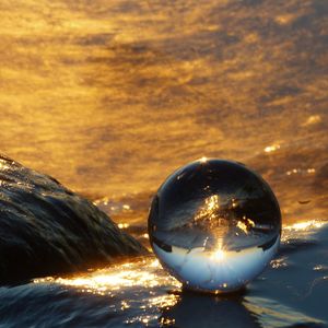 Close-up of crystal ball in sea against sunset sky