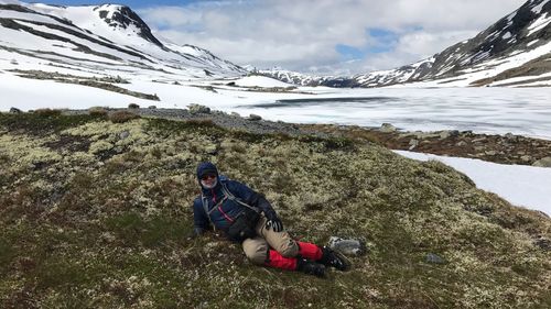 Man lying on grassy field against snowcapped mountains
