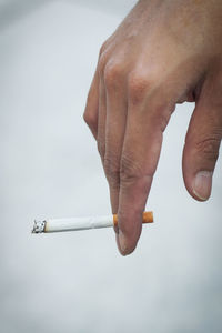 Close-up of hand holding cigarette against white background