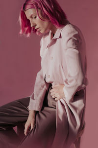 Young woman wearing coat while sitting against colored background