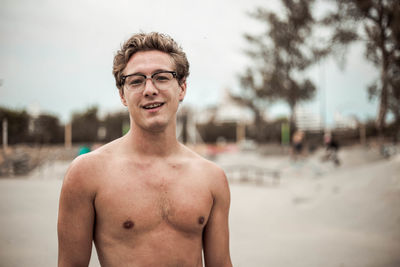 Portrait of smiling shirtless man standing at skate park