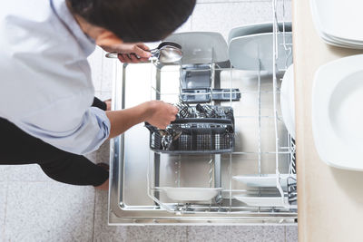 Woman removing or placing the cutlery in the dishwasher in the kitchen of her apartment.