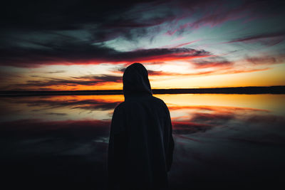 Silhouette man standing by lake with reflection of dramatic sky