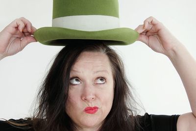 Woman holding green hat over her head against white background
