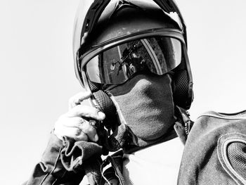 Low angle portrait of biker wearing helmet standing against clear sky