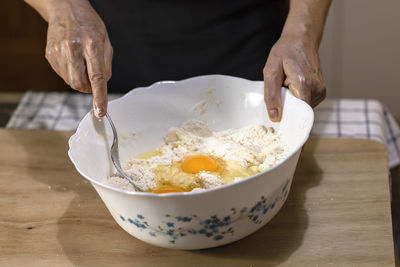 Midsection of person holding ice cream in bowl on table