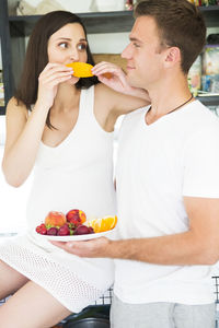 Man looking at pregnant woman eating fruit in kitchen