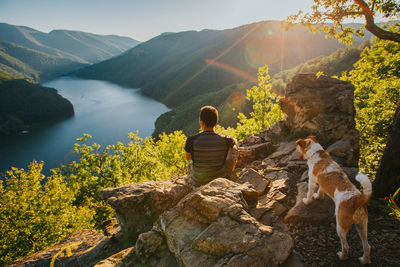 Rear view of man sitting on rock looking at mountains