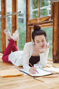 Woman drawing in book while lying on hardwood floor