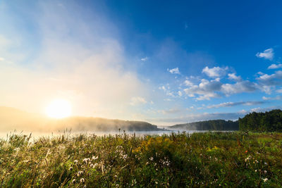 Scenic view of landscape against sky during foggy sunrise near river