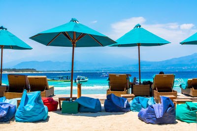 Parasols by lounge chairs and bean bags on sand at beach against sky