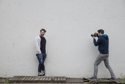 Full length of photographer photographing man leaning on wall