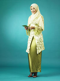 Woman in traditional clothing holding envelopes against green background