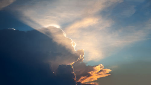 Low angle view of sunlight streaming through clouds