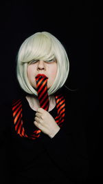 Portrait of mid adult woman with tie in mouth against black background