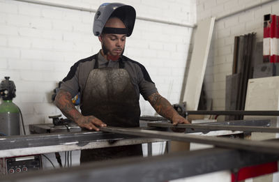 Serious male worker in dirty apron standing at workbench and preparing metal details for welding