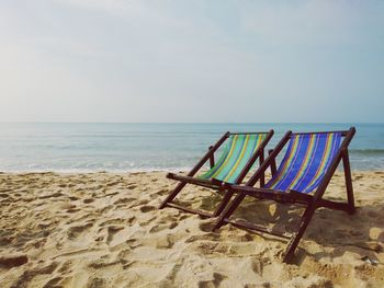 Deck chairs on beach against sky