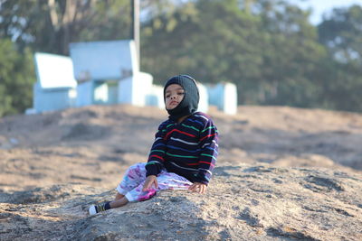 Full length of boy wearing warm clothes while sitting at beach