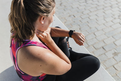 Female athlete looking at smart watch while checking pulse on neck during sunny day