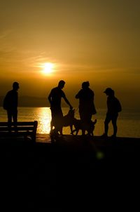 Silhouette people with dogs on wall during sunset