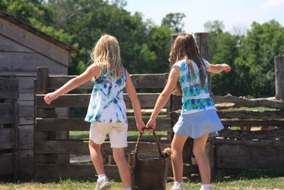 Rear view of sisters carrying bucket at yard