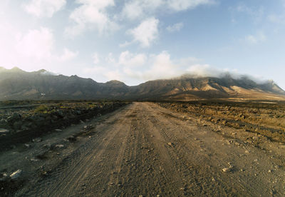 Dirt road leading towards mountains against sky