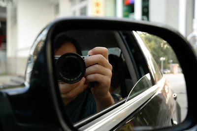 Close-up of man photographing car side-view mirror