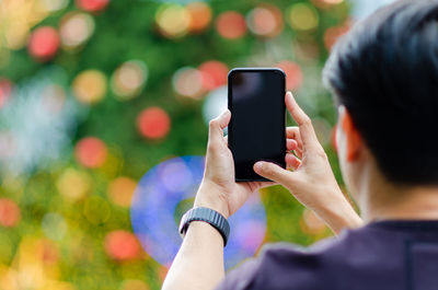 Asian man holding and taking christmas tree photo with smartphone to enjoy christmas holiday.