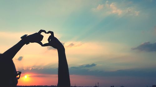 Silhouette man making heart shape against sky during sunset