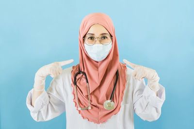 Portrait of doctor wearing hijab standing against blue background