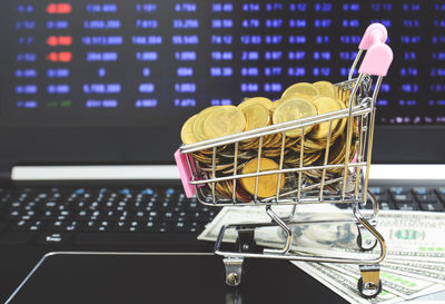 Close-up of coins in miniature shopping cart on laptop