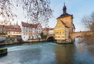 View of buildings by river against sky in city