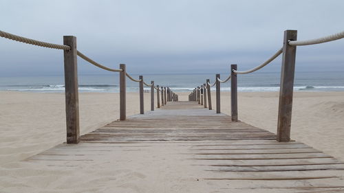 Wooden boardwalk leading towards sea against sky