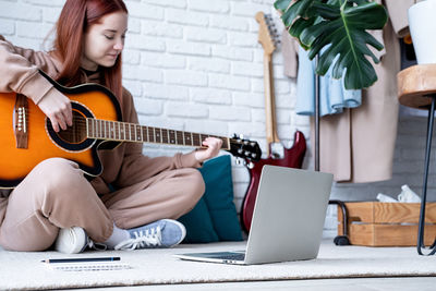 Man playing guitar while sitting on sofa at home