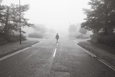 Rear view of young woman walking on road during foggy weather